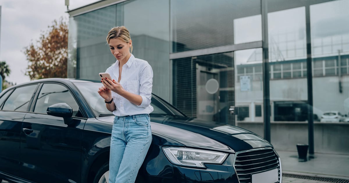 Une femme appuyée sur une voiture qui regarde son cellulaire