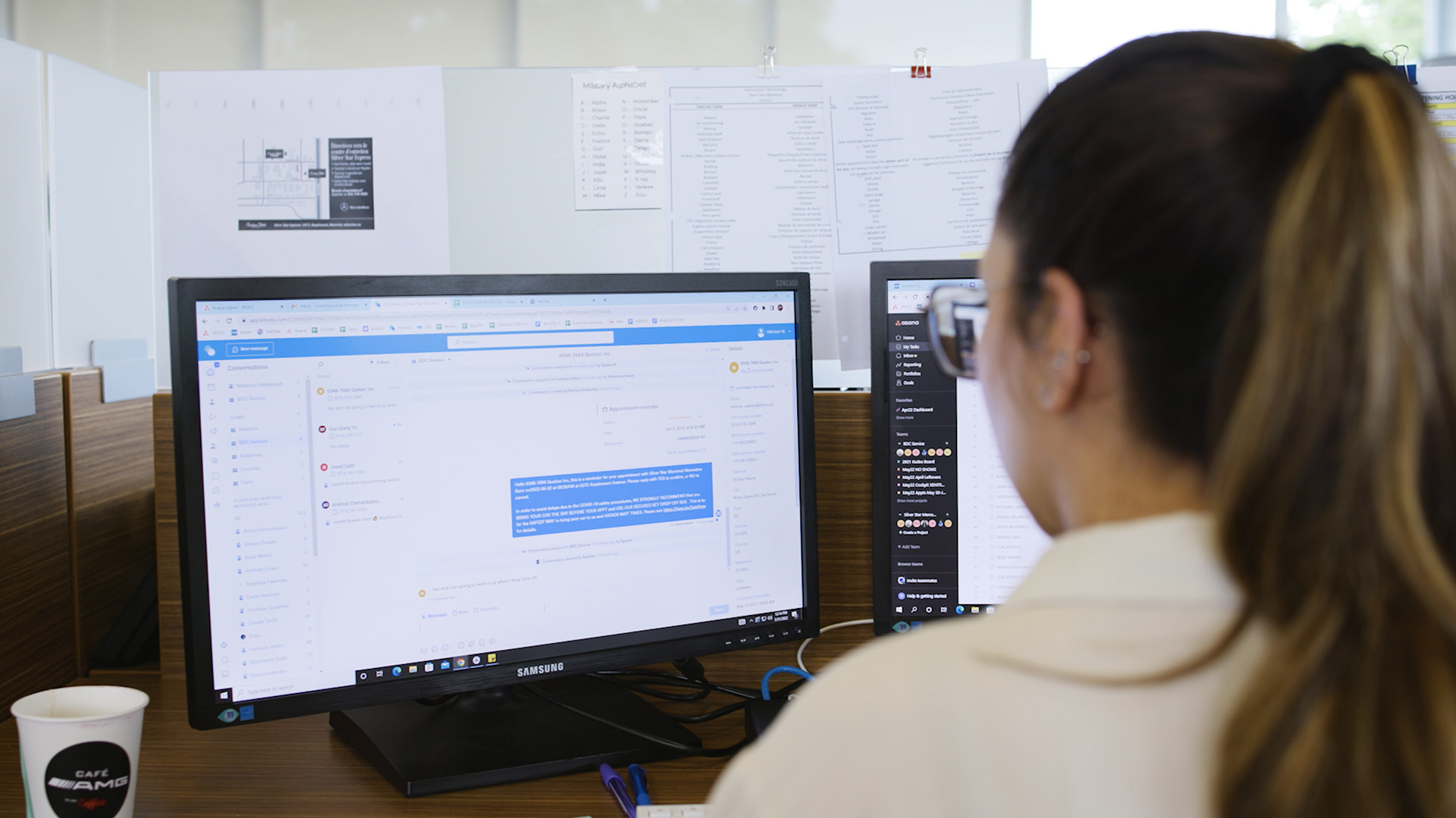 Person working at a desk with two monitors, showing Asana and messaging app.